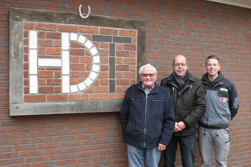 Drei Männer vor einer Ziegelwand mit HDT-Logo.