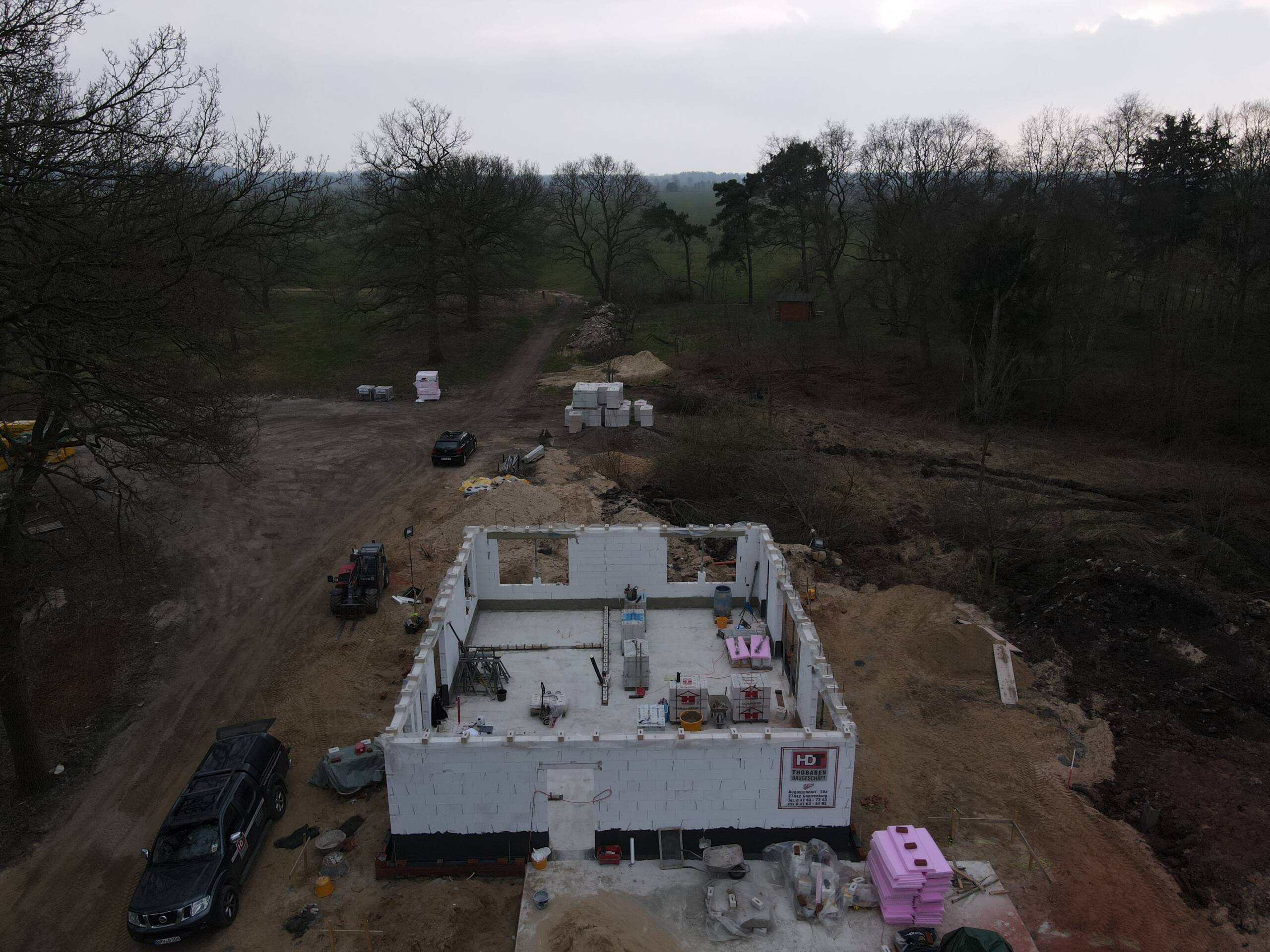 Drohnenbild eines Rohbaus im frühen Stadium, eingebettet in eine bewaldete Umgebung mit Baustellenfahrzeugen.