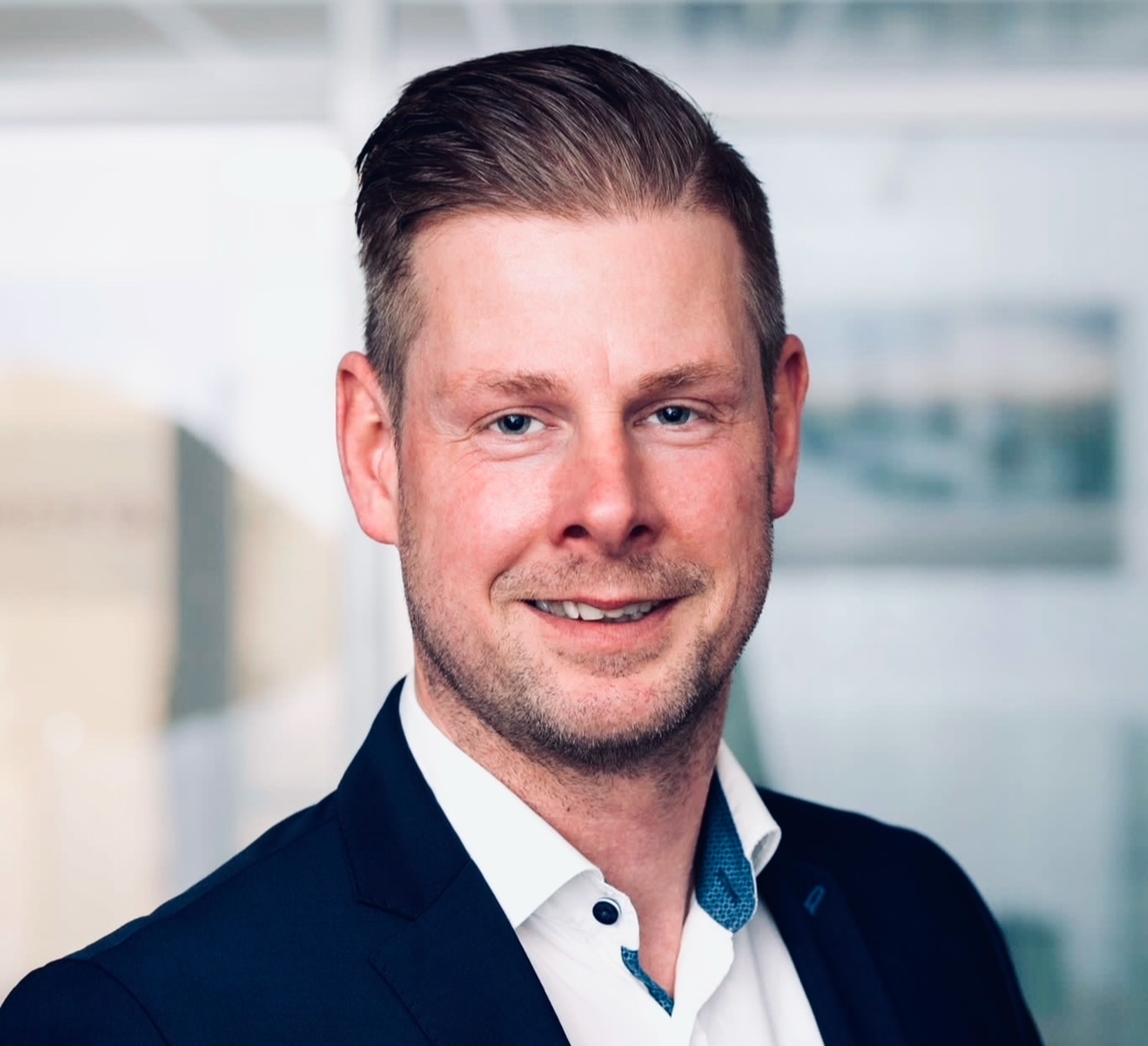 Porträt eines Mannes im Anzug vor unscharfem Hintergrund in Büroatmosphäre.