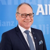 Fotografie eines Allianz Mitarbeiters im Anzug vor einem blauen Hintergrund.